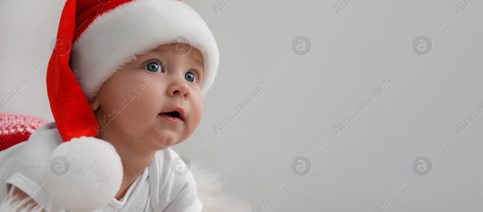 Image of Cute baby wearing Santa hat on light grey background, banner design with space for text. Christmas celebration