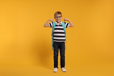 Photo of Happy schoolboy in glasses with backpack on orange background