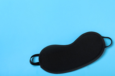 Black sleeping mask on light blue background, top view with space for text. Bedtime accessory