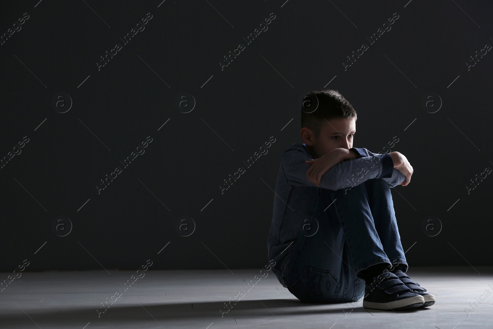 Photo of Upset boy sitting in dark room. Space for text