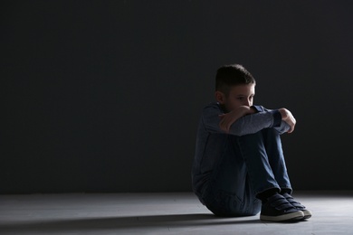 Upset boy sitting in dark room. Space for text