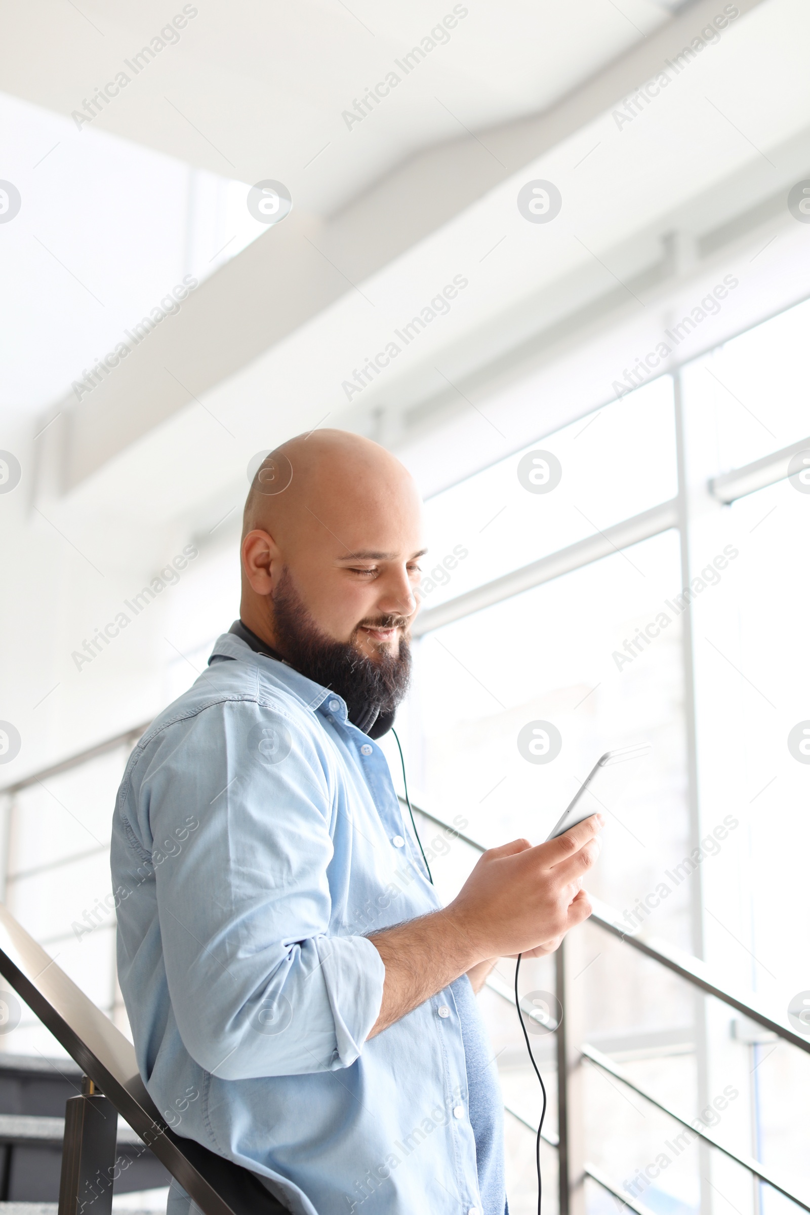Photo of Portrait of young man with mobile phone and headphones on stairs