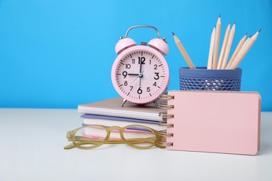 Photo of Different school stationery, alarm clock and glasses on white table against light blue background, space for text. Back to school
