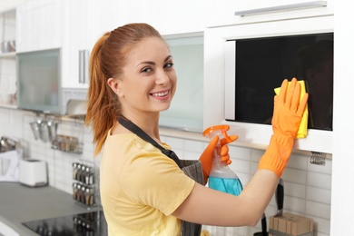 Photo of Woman cleaning microwave oven with rag and detergent in kitchen