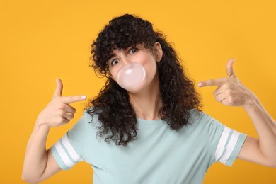 Photo of Beautiful young woman blowing bubble gum on orange background