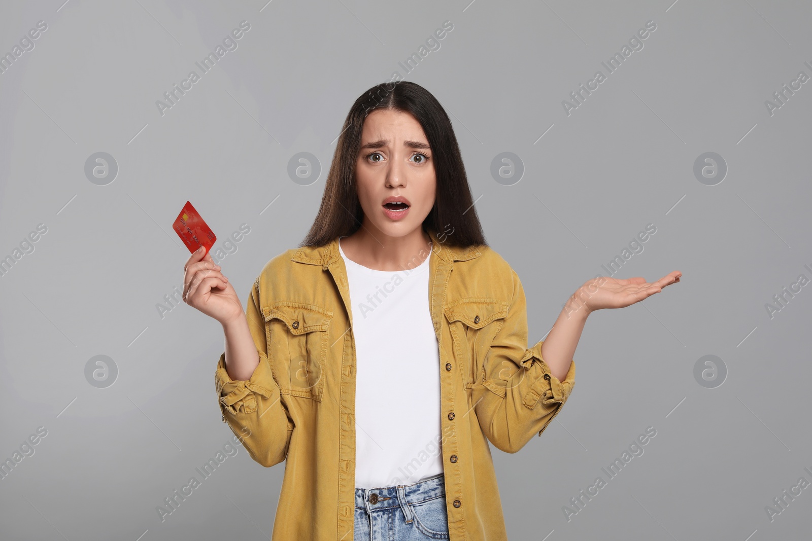 Photo of Shocked woman with credit card on light gray background. Debt problem