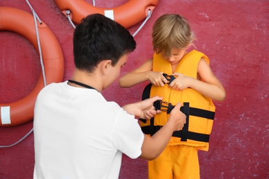 Photo of Rescuer putting orange life vest on child near red wall
