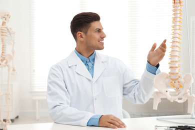 Male orthopedist at table near human spine model in office