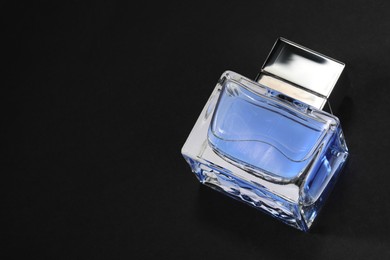 Photo of Blue men's perfume in bottle on black background, above view. Space for text