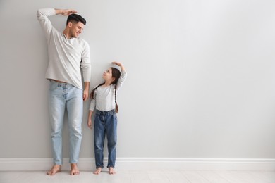 Photo of Little girl and father measuring their height near light grey wall indoors. Space for text