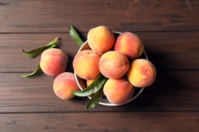 Plate with fresh sweet peaches on wooden table, top view