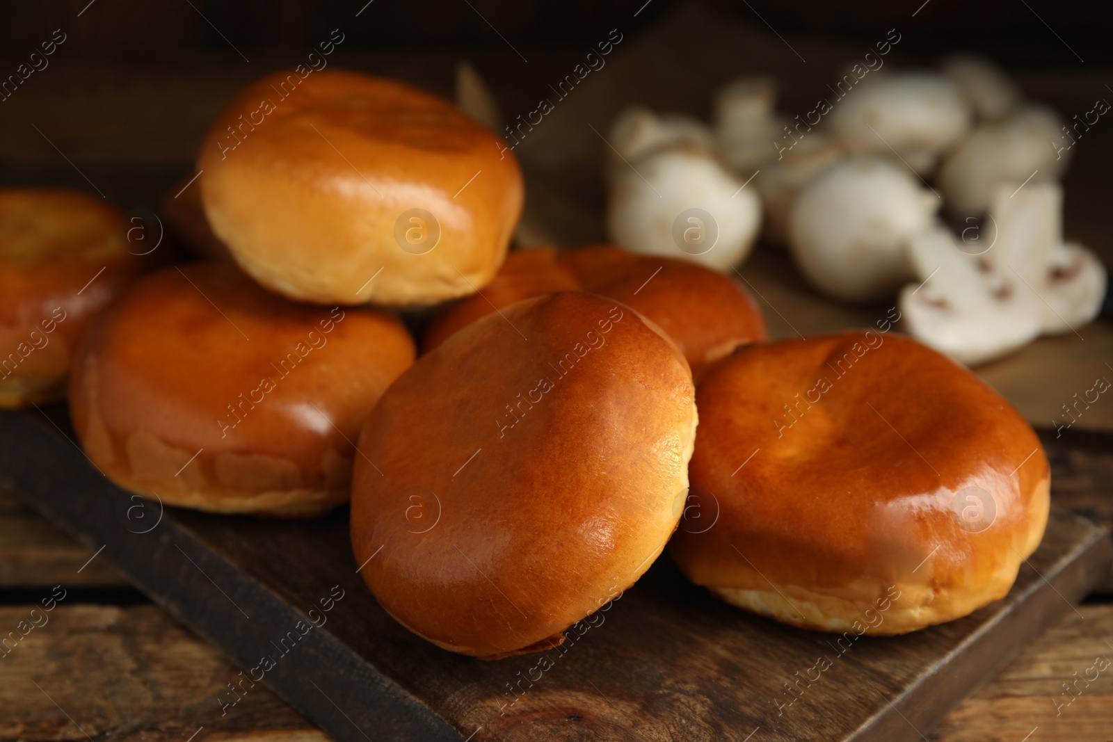 Photo of Delicious baked mushrooms pirozhki on wooden board, closeup