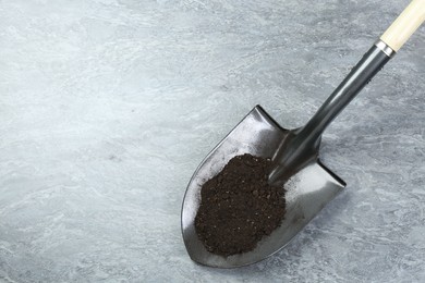 Photo of Metal shovel with fertile soil on gray background, above view. Space for text