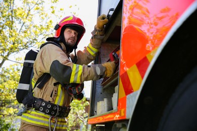 Firefighter in uniform with helmet near fire truck outdoors