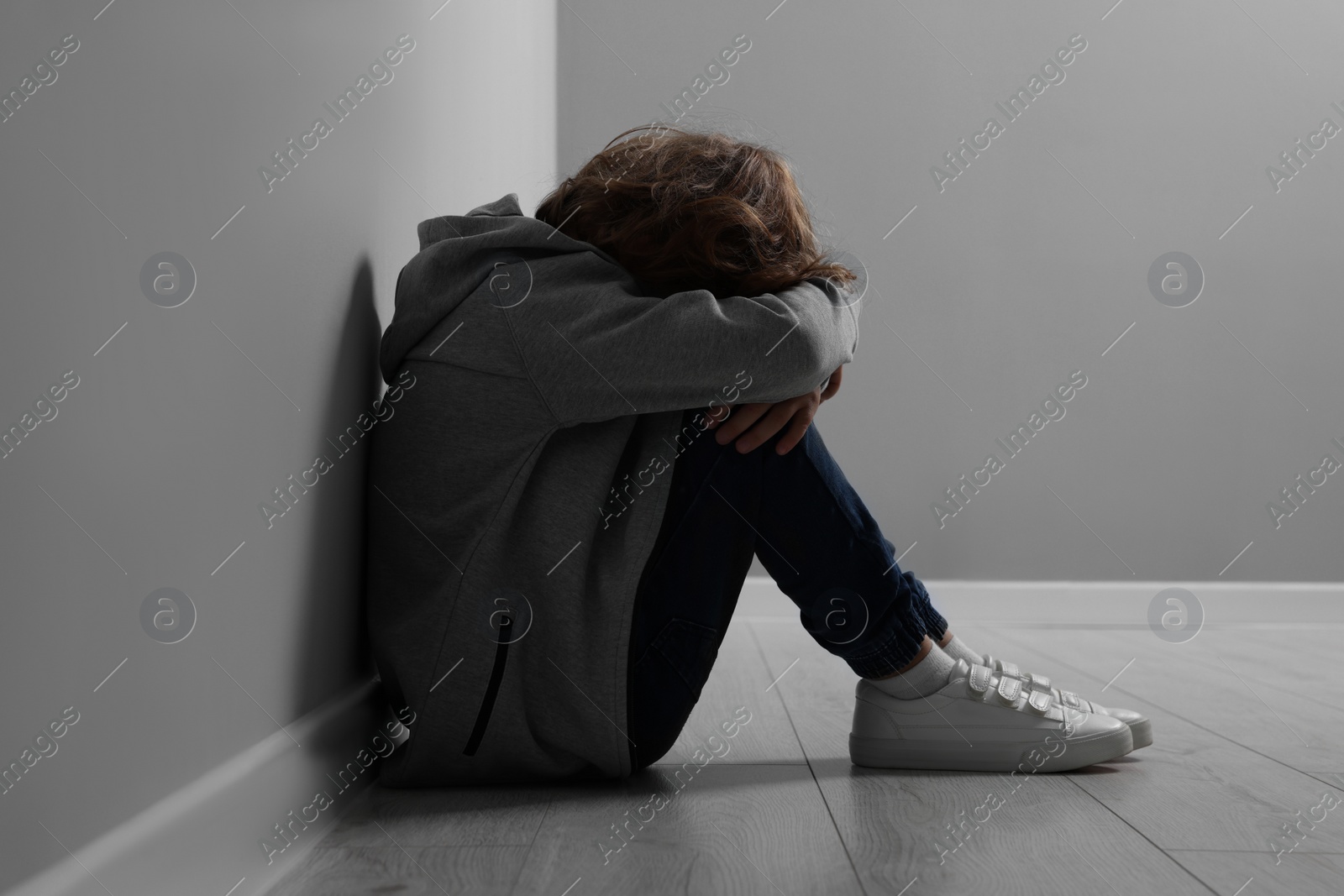 Photo of Child abuse. Upset boy sitting on floor near grey wall