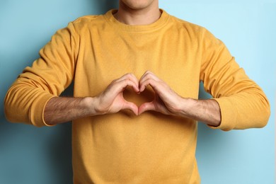 Man making heart with hands on light blue background, closeup