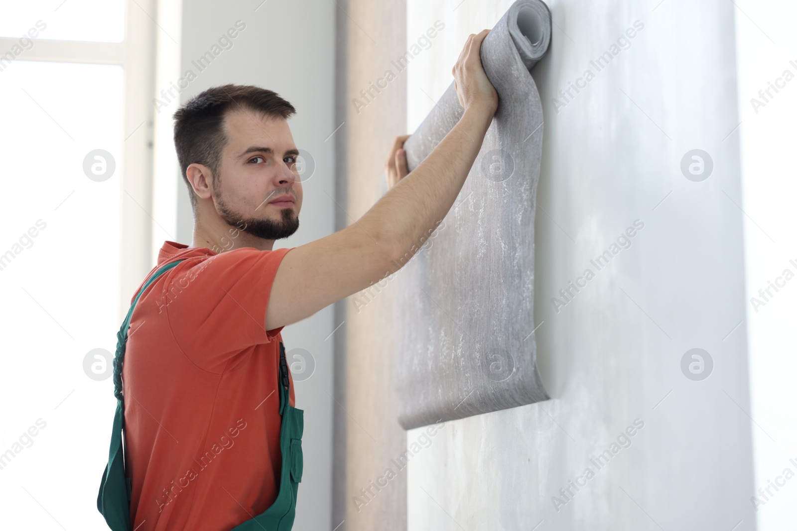 Photo of Man hanging stylish gray wallpaper in room