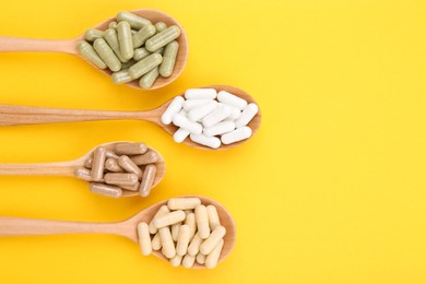 Photo of Different vitamin capsules in wooden spoons on yellow background, flat lay. Space for text