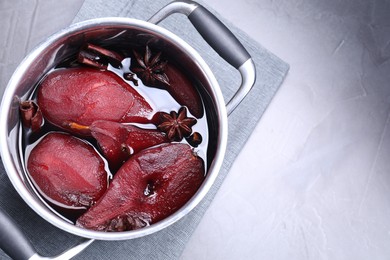 Tasty red wine poached pears and spices in pot on grey table, top view. Space for text