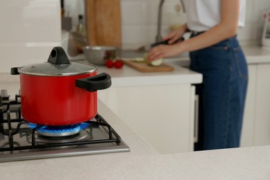 Photo of Woman cooking food in kitchen, focus on gas stove with red pot