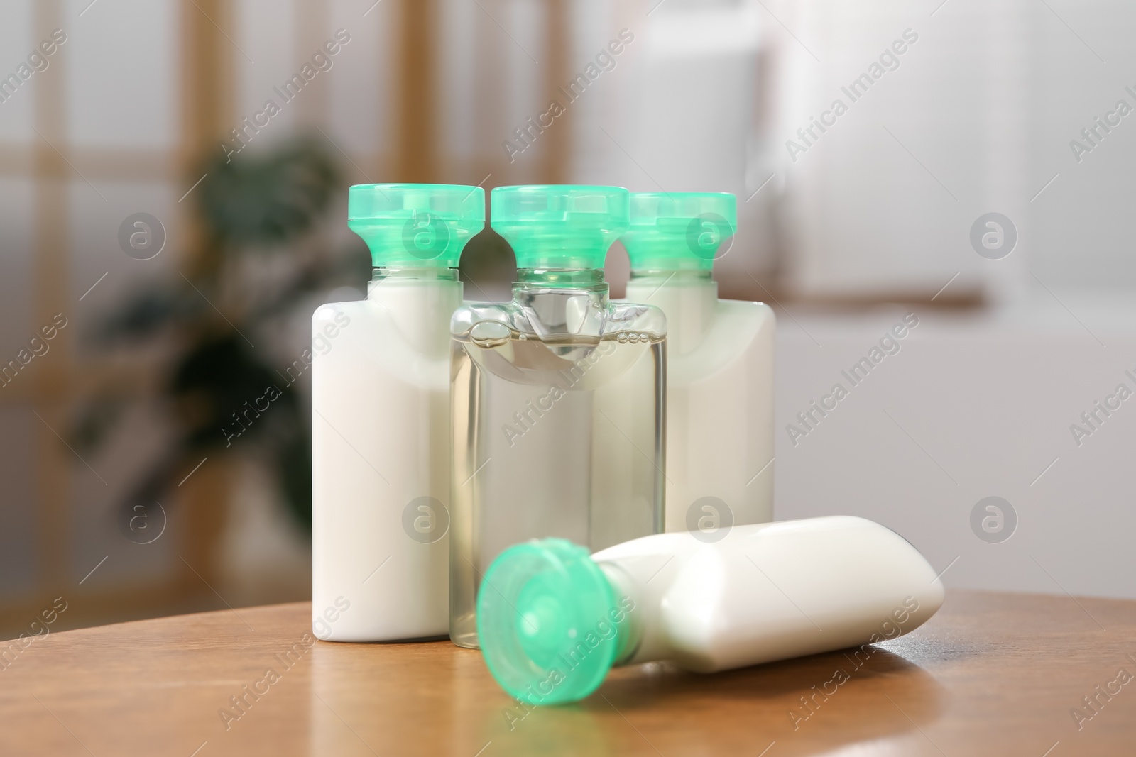 Photo of Mini bottles of cosmetic products and green branch on wooden table against blurred background