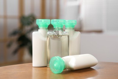 Mini bottles of cosmetic products and green branch on wooden table against blurred background