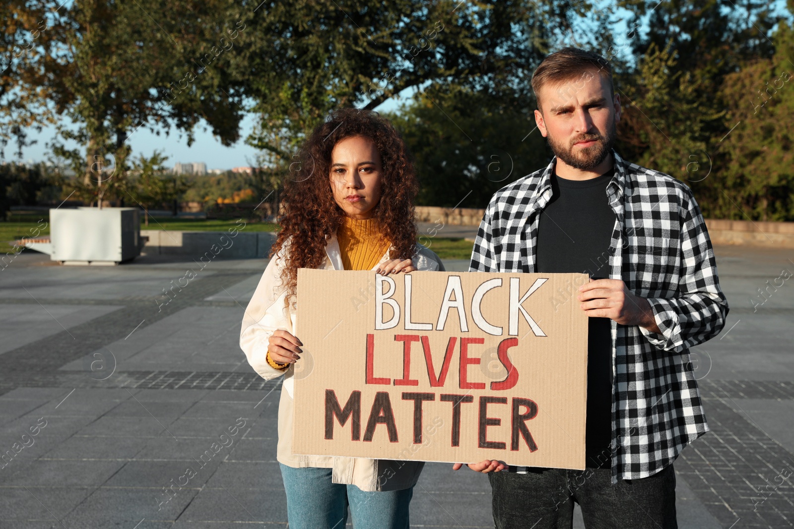Photo of Young man and African American woman holding sign with phrase Black Lives Matter outdoors. Racism concept