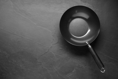 Photo of Empty iron wok on black textured table, top view. Space for text