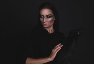 Photo of Mysterious witch with raven on black background