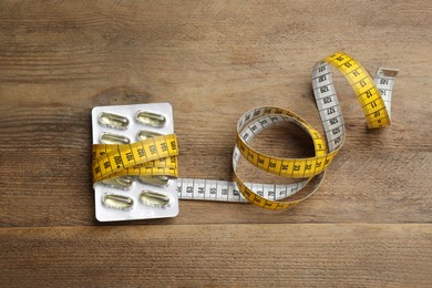 Photo of Oil capsules and measuring tape on wooden table, flat lay. Weight loss