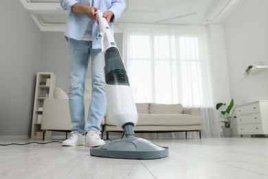 Photo of Man cleaning floor with steam mop at home, closeup