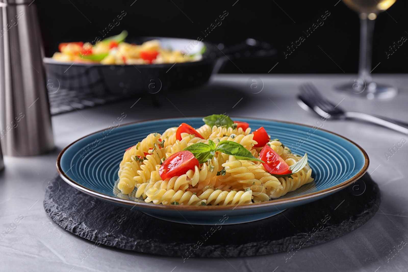 Photo of Delicious pasta with tomatoes and basil served on grey table
