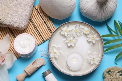 Photo of Beautiful composition with spa products, burning candle and flowers on light blue background, flat lay