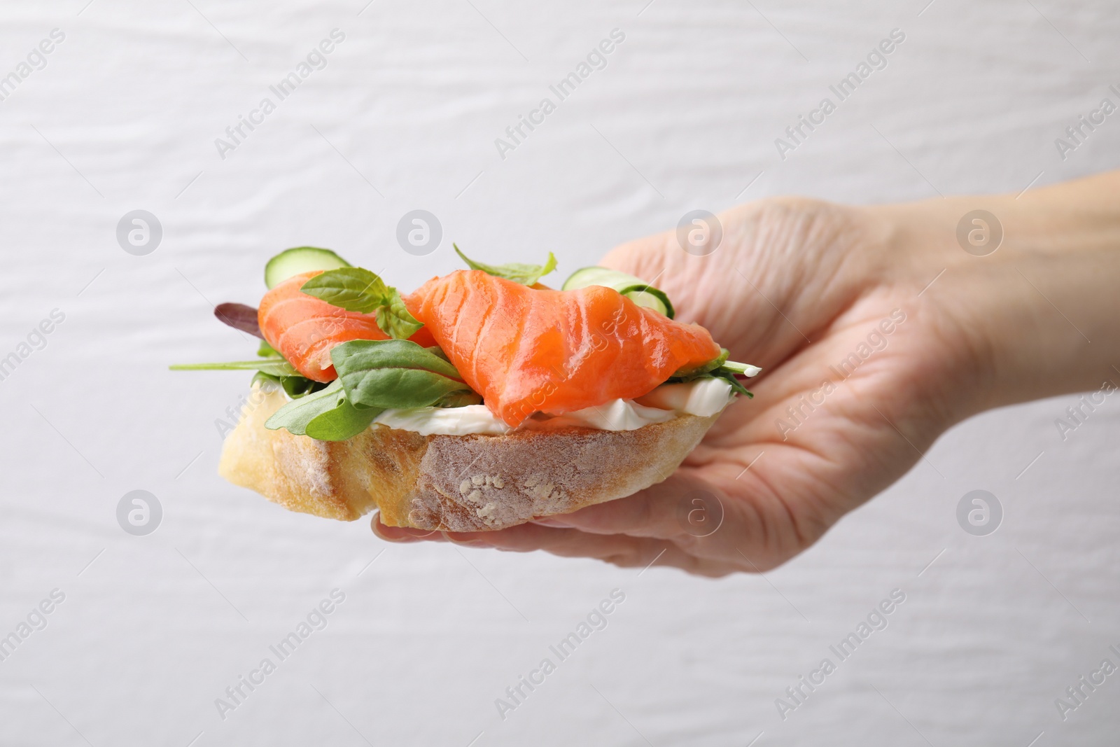Photo of Woman holding tasty bruschetta with salmon against white wall, closeup