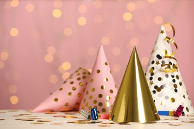 Photo of Party hats and festive items on white table against pink background with blurred lights. Space for text