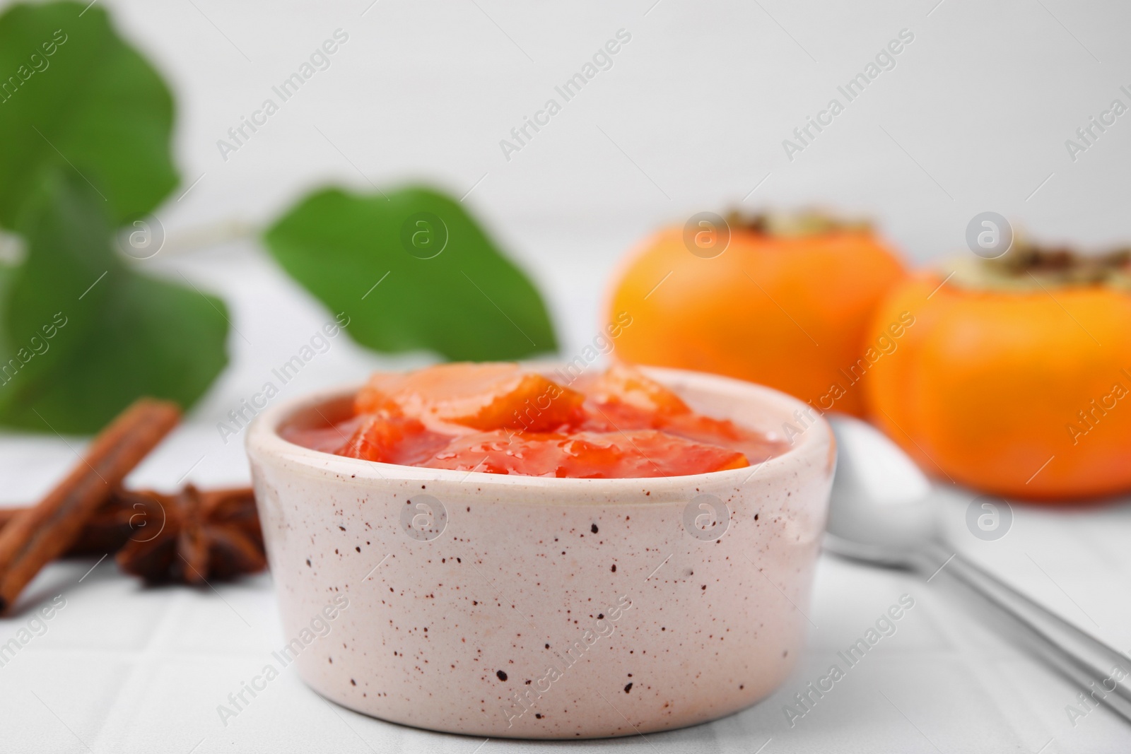 Photo of Bowl of tasty persimmon jam on white tiled table, closeup