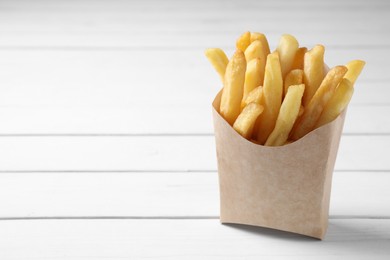 Delicious french fries in paper box on white wooden table, space for text