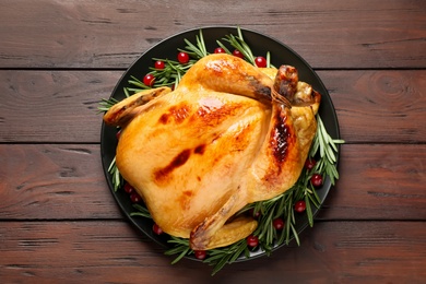 Photo of Delicious cooked turkey served with rosemary and cranberries on wooden table, top view. Thanksgiving Day celebration