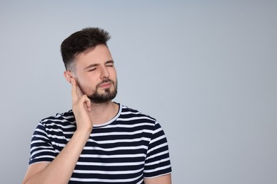 Young man suffering from ear pain on light grey background. Space for text