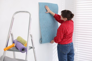 Photo of Woman hanging light blue wallpaper in room