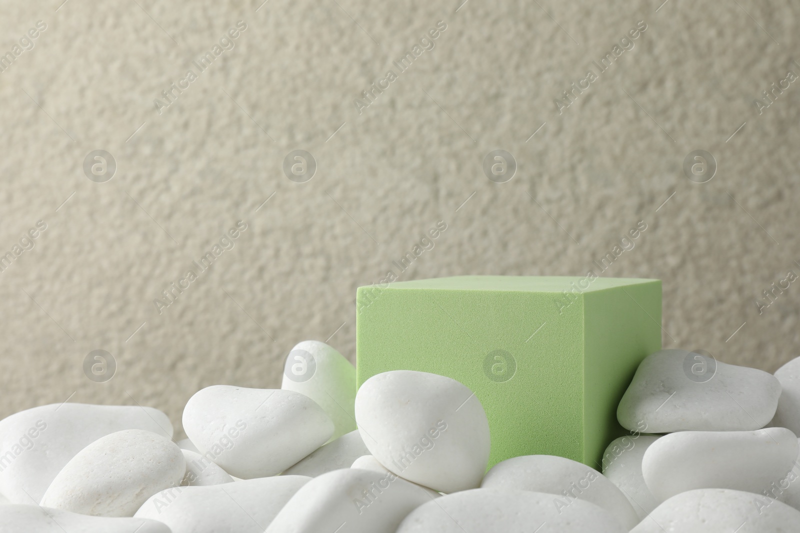 Photo of Presentation for product. Light green cube podium and white pebbles on blurred background. Space for text