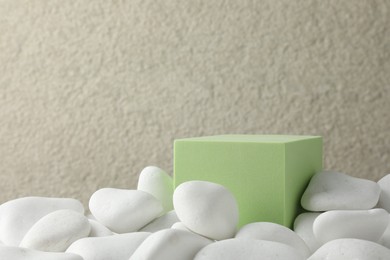 Presentation for product. Light green cube podium and white pebbles on blurred background. Space for text