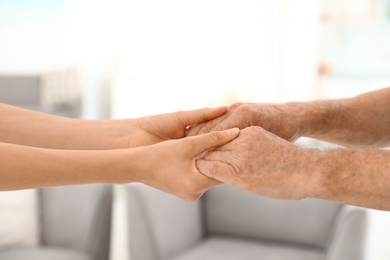 People holding hands together on blurred background, closeup. Help and elderly care concept