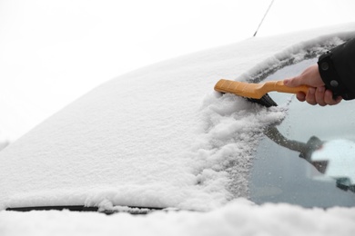 Man cleaning car windshield from snow with brush outdoors, closeup