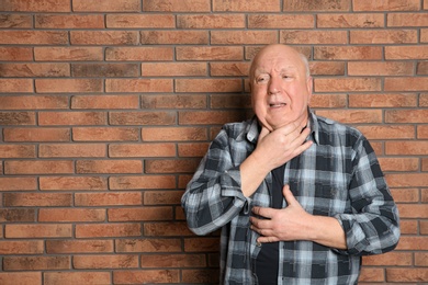 Photo of Senior man suffering from cough near brick wall. Space for text