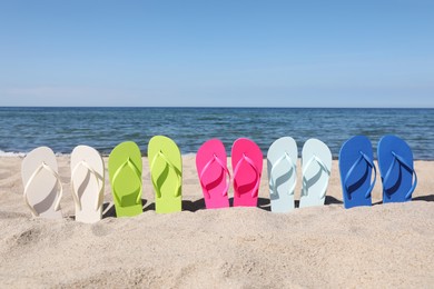 Many stylish colorful flip flops on beach sand