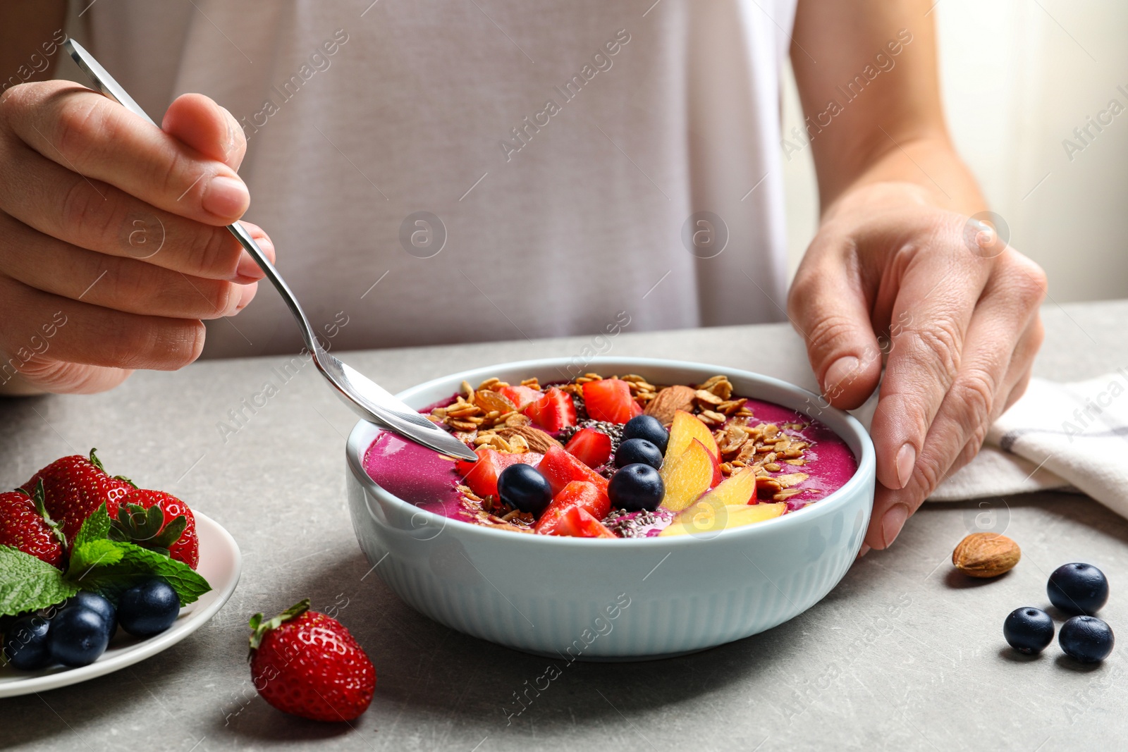 Photo of Woman eating delicious acai smoothie at grey table, closeup