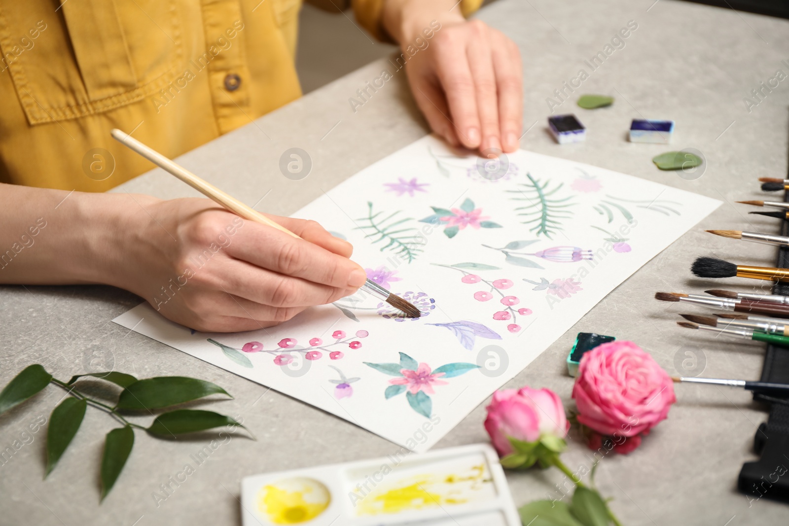 Photo of Woman painting flowers with watercolor at grey stone table, closeup