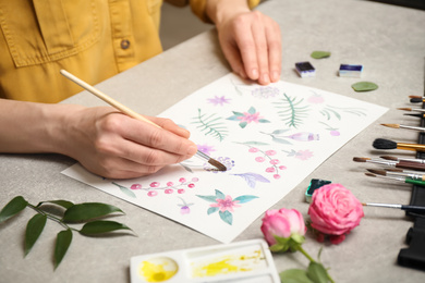 Photo of Woman painting flowers with watercolor at grey stone table, closeup