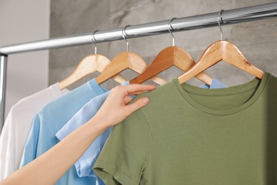Photo of Woman hanging clean T-shirts on rack indoors, closeup